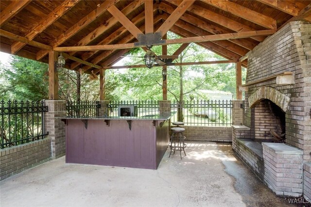 view of patio with a gazebo, an outdoor brick fireplace, ceiling fan, and a bar