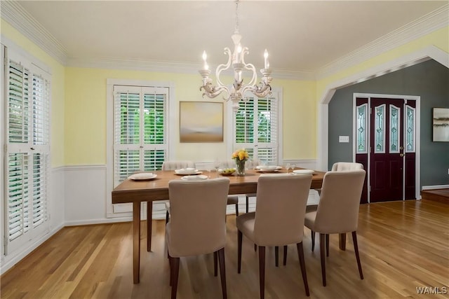 dining area with wood-type flooring, ornamental molding, and a chandelier