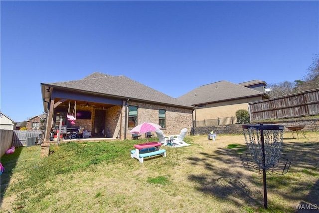 rear view of property with brick siding, a fenced backyard, a lawn, and a patio