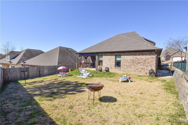 rear view of property featuring an outdoor fire pit, a fenced backyard, brick siding, and a lawn