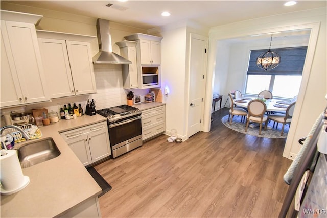 kitchen with wall chimney range hood, light wood-type flooring, a sink, and stainless steel gas range oven