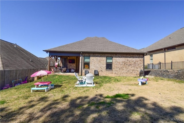 back of house featuring a patio, brick siding, fence, a lawn, and roof with shingles