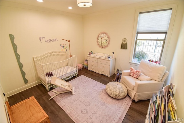 bedroom with a nursery area, dark wood-style flooring, baseboards, and crown molding