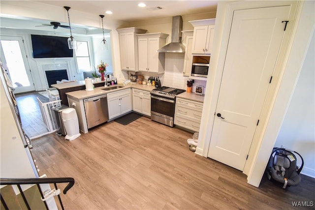 kitchen with light wood finished floors, stainless steel appliances, open floor plan, a sink, and wall chimney range hood