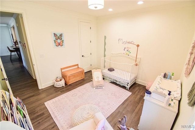 bedroom with baseboards, dark wood-style floors, crown molding, a nursery area, and recessed lighting