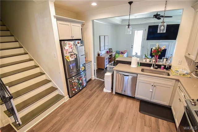 kitchen featuring stainless steel appliances, a sink, white cabinetry, hanging light fixtures, and light wood-type flooring