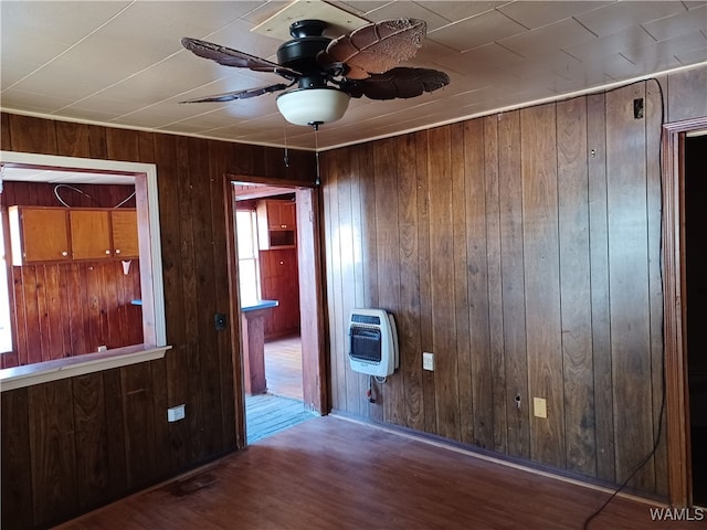 unfurnished room featuring hardwood / wood-style flooring, ceiling fan, wooden walls, and heating unit