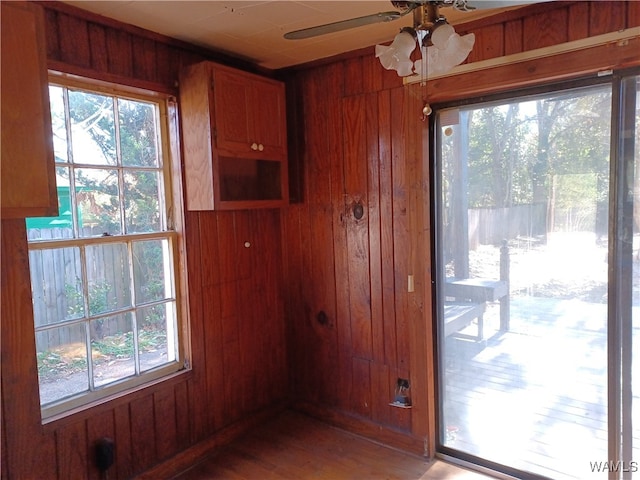 doorway with hardwood / wood-style floors, wooden walls, ceiling fan, and a healthy amount of sunlight