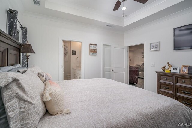 bedroom with ornamental molding, ensuite bathroom, ceiling fan, and a tray ceiling