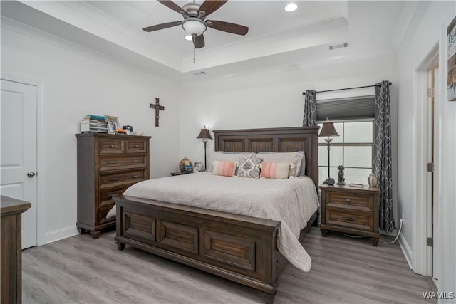 bedroom with crown molding, a tray ceiling, ceiling fan, and light wood-type flooring