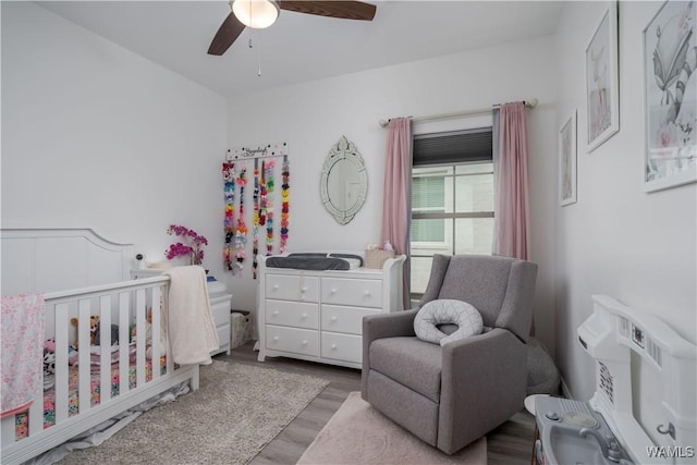 bedroom featuring ceiling fan, light hardwood / wood-style floors, and a crib