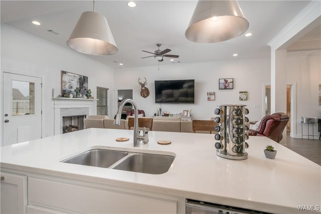 kitchen featuring sink, ceiling fan, white cabinetry, hanging light fixtures, and ornamental molding