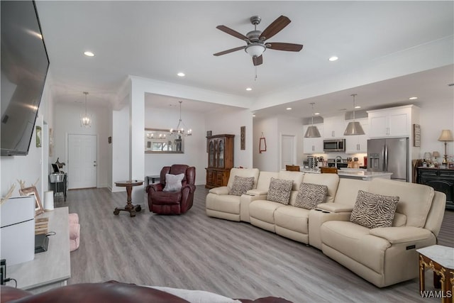 living room with ornamental molding, ceiling fan with notable chandelier, and light hardwood / wood-style flooring