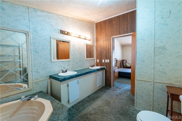 bathroom with a tub to relax in, a textured ceiling, wooden walls, vanity, and ornamental molding