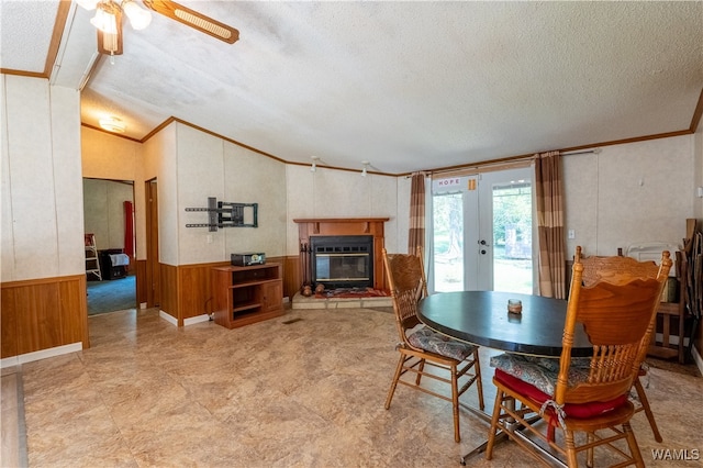 dining area featuring french doors, crown molding, wooden walls, ceiling fan, and a textured ceiling