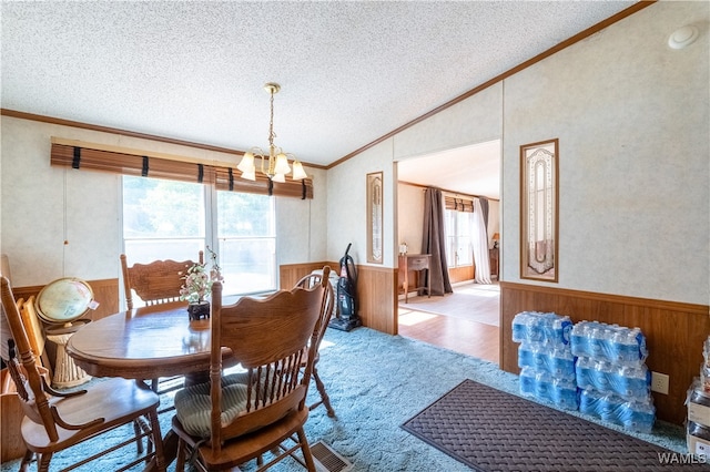 carpeted dining space featuring wood walls, vaulted ceiling, ornamental molding, a textured ceiling, and a chandelier