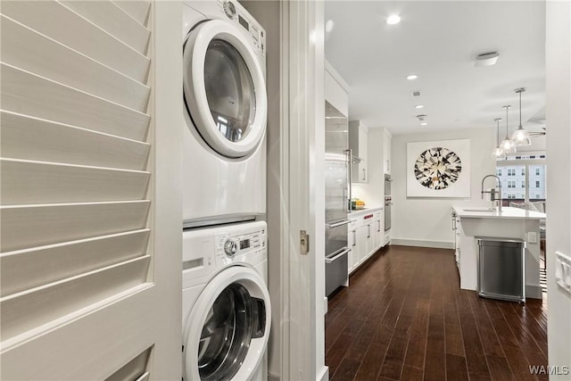 washroom featuring stacked washer and clothes dryer, sink, and dark wood-type flooring