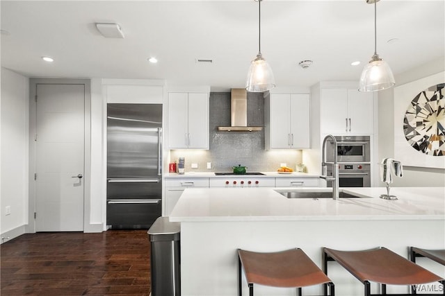 kitchen featuring appliances with stainless steel finishes, pendant lighting, white cabinets, and wall chimney exhaust hood