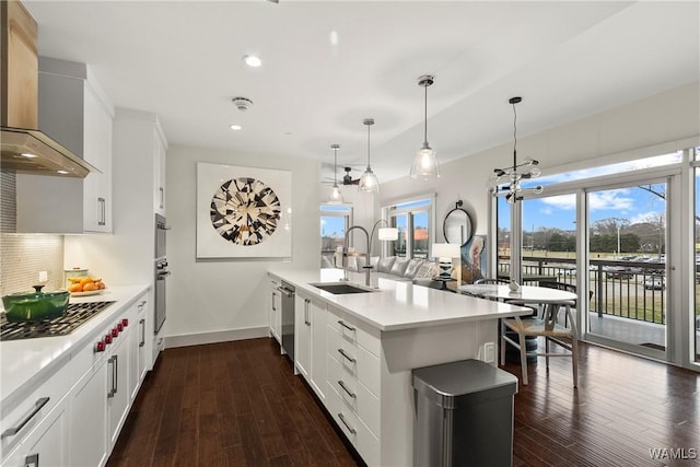 kitchen with sink, white cabinetry, hanging light fixtures, kitchen peninsula, and wall chimney range hood