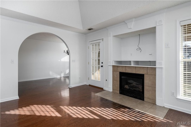 unfurnished living room featuring a tiled fireplace, a wealth of natural light, and dark wood-type flooring