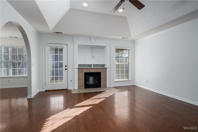 unfurnished living room featuring dark hardwood / wood-style flooring, vaulted ceiling, a raised ceiling, ceiling fan, and a tiled fireplace