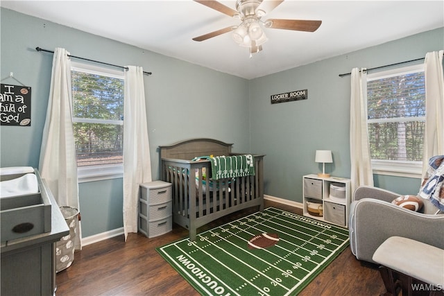 bedroom with multiple windows, ceiling fan, dark wood-type flooring, and a nursery area