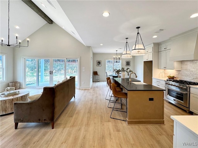 kitchen featuring stainless steel stove, white cabinetry, a kitchen island with sink, an inviting chandelier, and decorative light fixtures