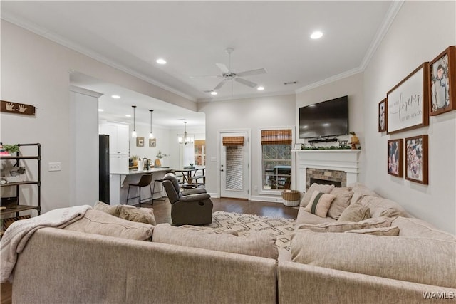 living room featuring crown molding, dark hardwood / wood-style floors, ceiling fan with notable chandelier, and a fireplace