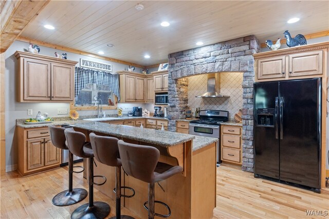 kitchen featuring a kitchen bar, light hardwood / wood-style floors, wall chimney range hood, and appliances with stainless steel finishes