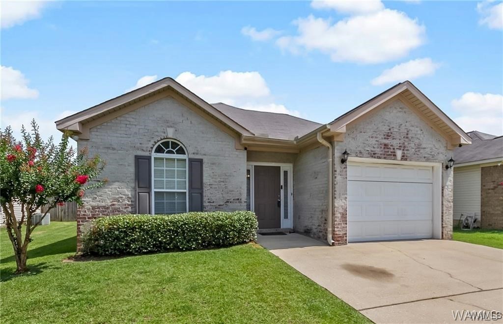 ranch-style home with a garage, a front yard, brick siding, and driveway