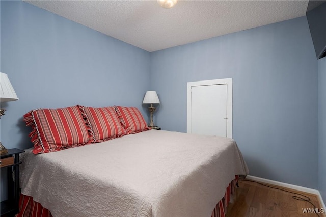 bedroom with a textured ceiling, baseboards, and wood finished floors