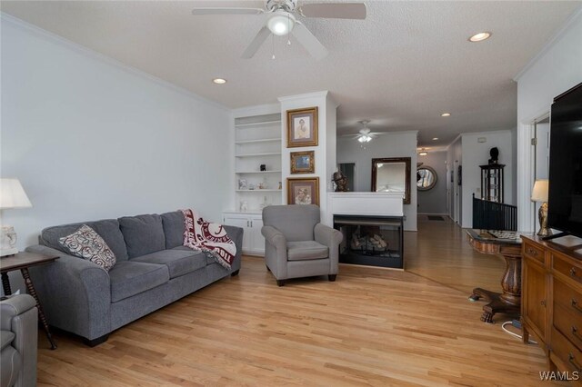 living room with crown molding, light wood-style flooring, built in shelves, and a fireplace