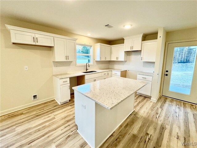 kitchen featuring visible vents, light wood-style flooring, a sink, a center island, and baseboards