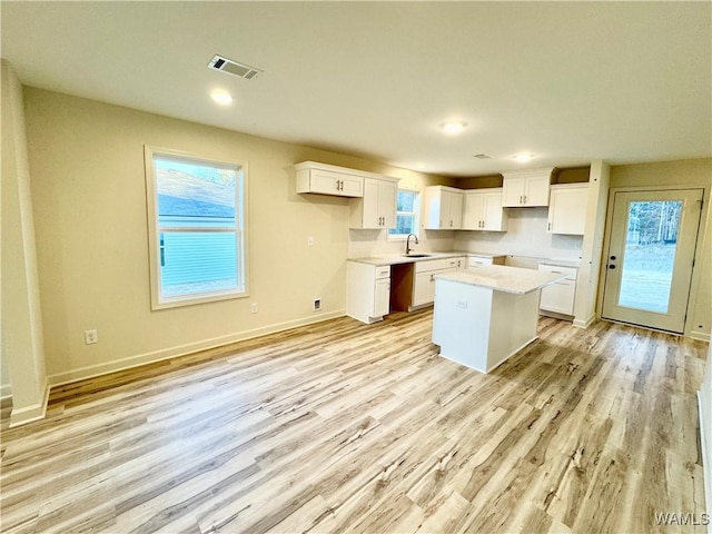 kitchen featuring visible vents, a kitchen island, light wood-style flooring, a sink, and white cabinetry