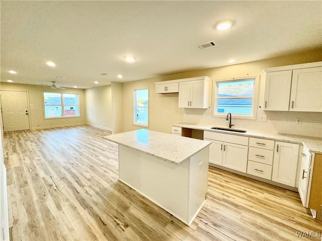 kitchen with visible vents, a kitchen island, a sink, white cabinets, and light wood-type flooring