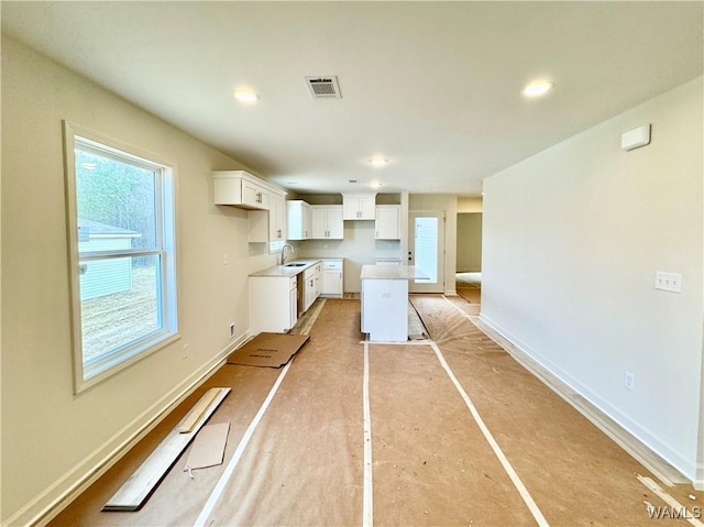 kitchen with visible vents, white cabinets, baseboards, and a sink