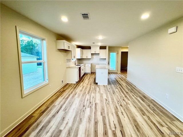 kitchen with baseboards, visible vents, light wood-style flooring, a sink, and white cabinetry