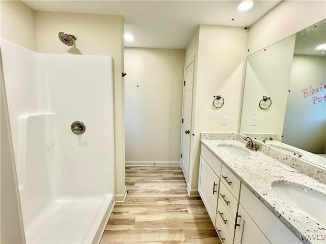 full bath featuring wood finished floors, a walk in shower, double vanity, and a sink