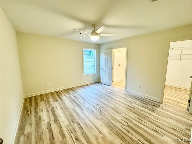 unfurnished bedroom featuring a walk in closet, ensuite bath, baseboards, and light wood-type flooring