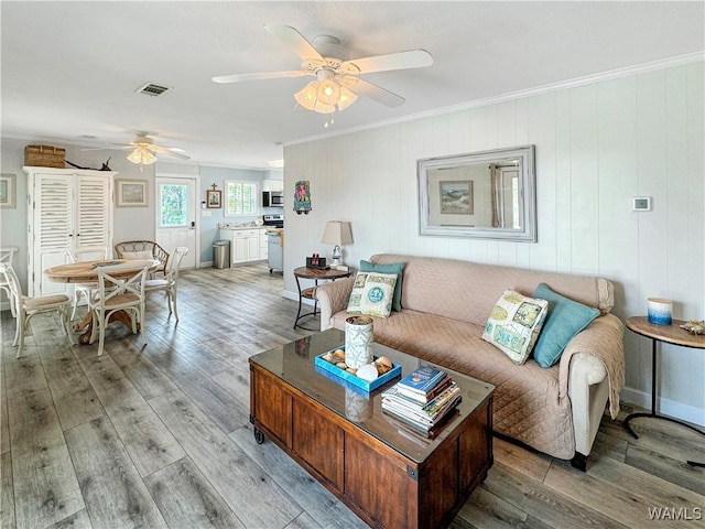 living area with visible vents, light wood-style flooring, crown molding, and ceiling fan