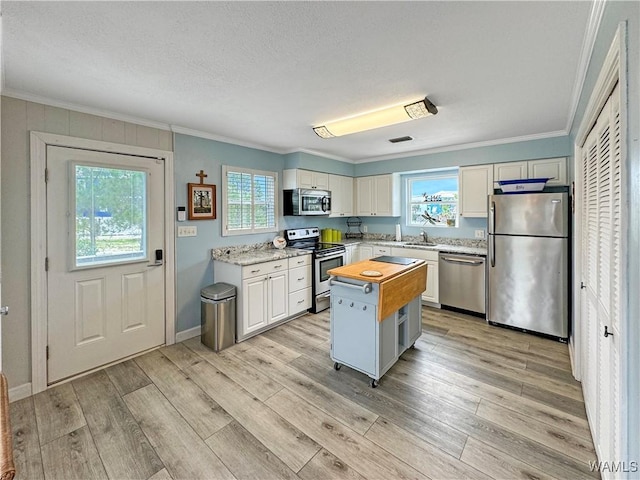 kitchen with ornamental molding, stainless steel appliances, light wood-style floors, wood counters, and white cabinetry