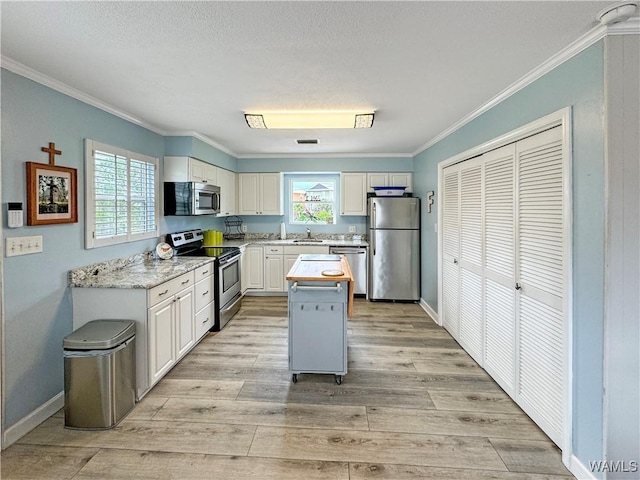 kitchen featuring ornamental molding, light wood-style flooring, a sink, white cabinetry, and stainless steel appliances