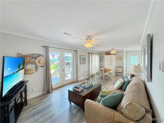 living area featuring visible vents, light wood-style floors, french doors, a textured ceiling, and crown molding