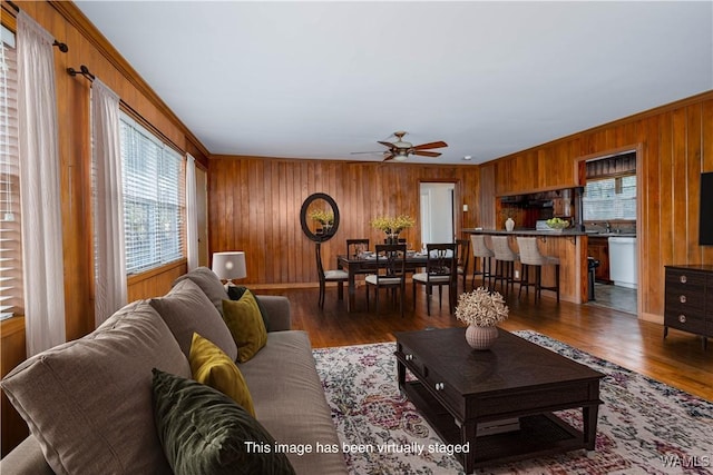 living room with ceiling fan, wooden walls, and wood finished floors