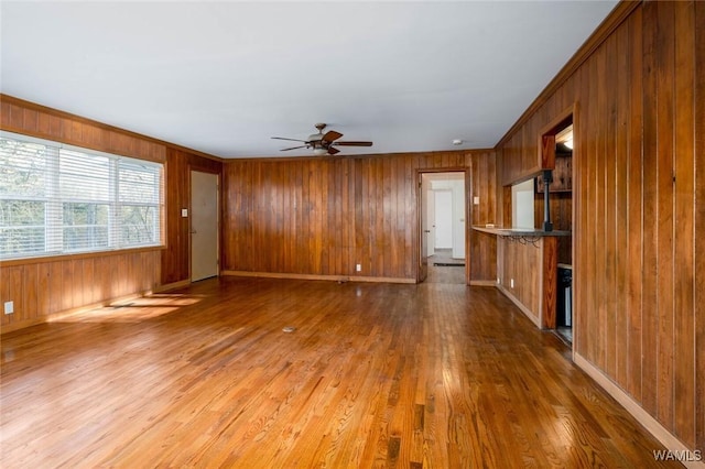 unfurnished living room with a ceiling fan, wood finished floors, baseboards, and wood walls