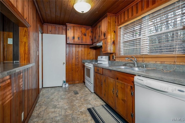 kitchen with a sink, white appliances, wooden walls, and under cabinet range hood