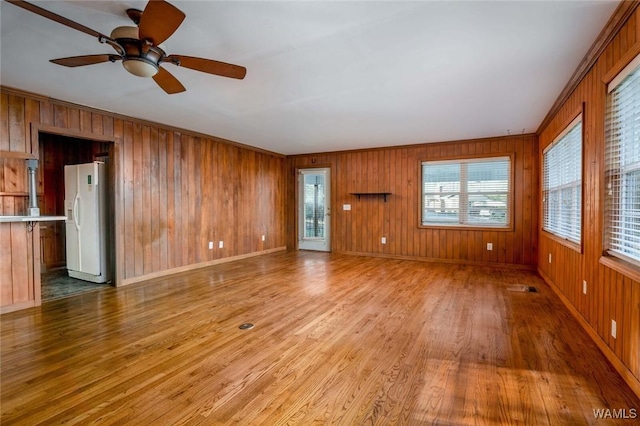 unfurnished living room featuring wooden walls, baseboards, light wood finished floors, ornamental molding, and ceiling fan