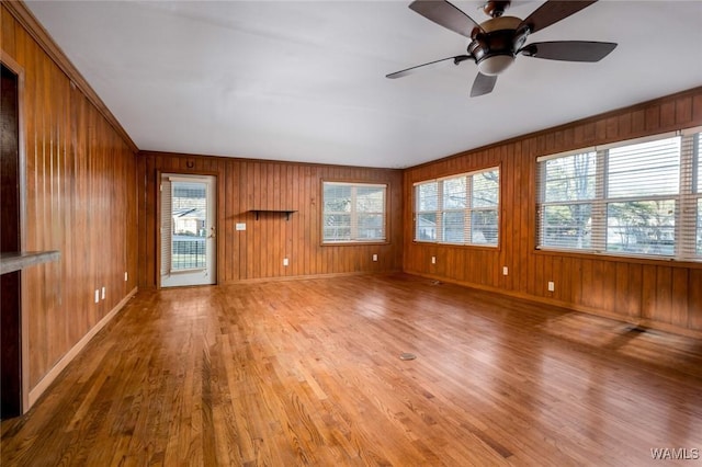 unfurnished living room featuring baseboards, light wood-style flooring, a ceiling fan, and wood walls