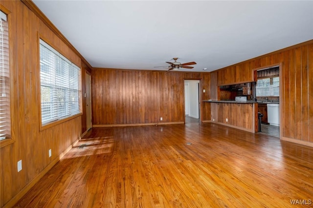 unfurnished living room featuring light wood-style floors, baseboards, wood walls, and ceiling fan