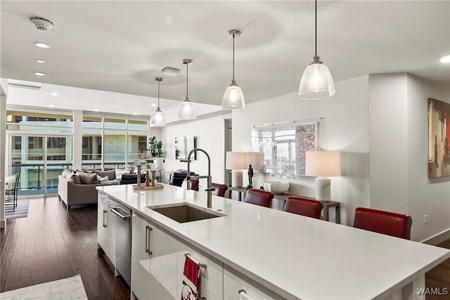 kitchen featuring a kitchen island with sink, sink, decorative light fixtures, white cabinets, and dark hardwood / wood-style floors